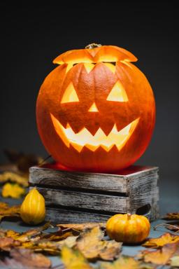 Jack o lantern on wooden block surrounded by leaves a gourdes