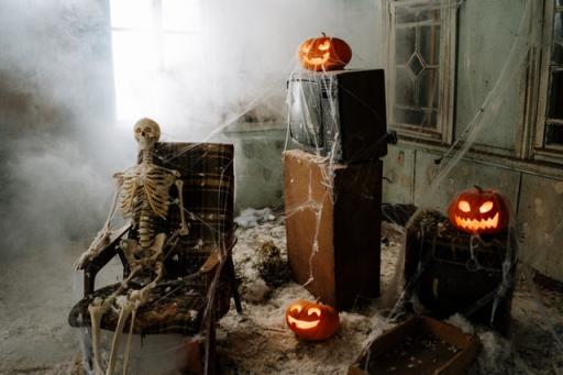 Full sized Halloween skeleton sitting in a chair with cobwebs and 3 pumpkins